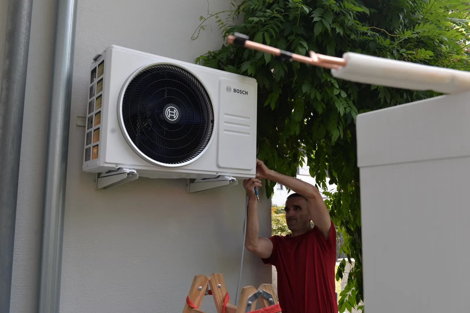 Monteur der Elektro-Service SFS montiert das Außengerät einer Klimaanlage an einer Hauswand